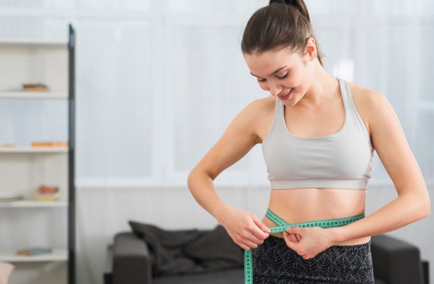 Woman measuring waist with tape at home.